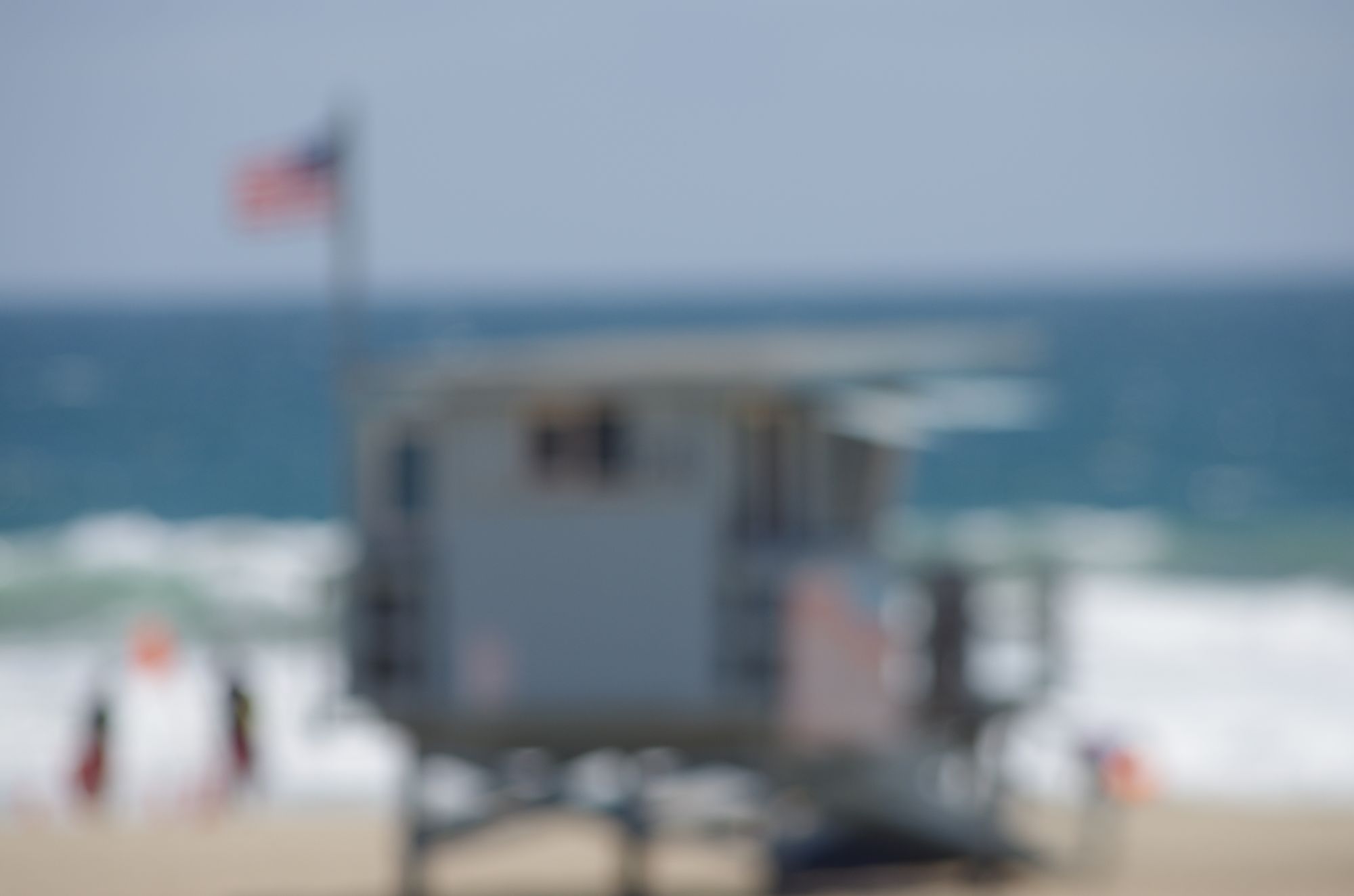 A lifeguard tower and a flag by the ocean, out of focus