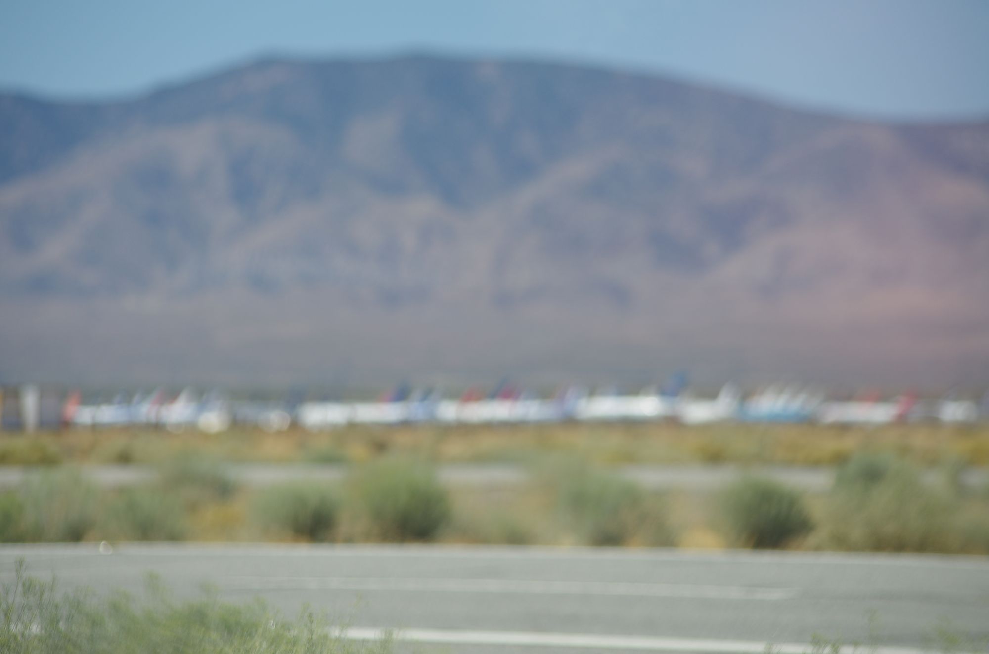A row of airplanes in the desert below a mountain, out of focus