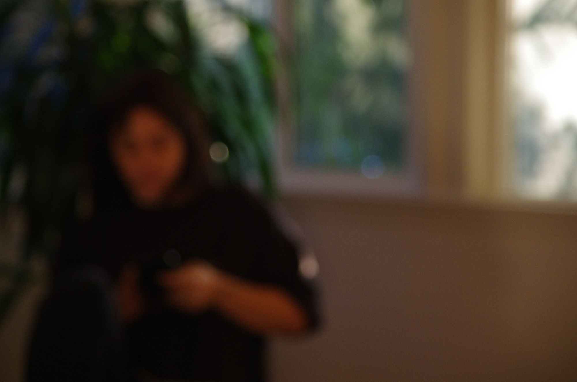 A woman holding a camera near a plant, out of focus