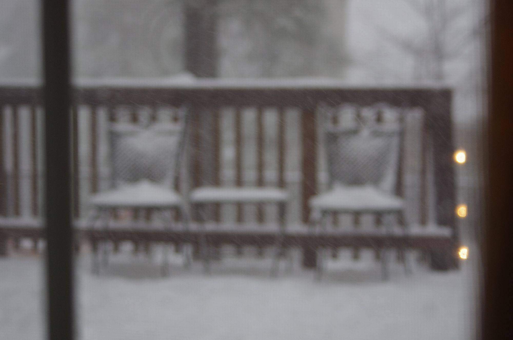 Two chairs on a porch under falling snow, out of focus